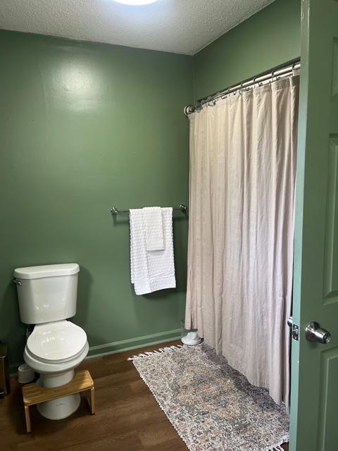 bathroom with baseboards, toilet, a shower with curtain, wood finished floors, and a textured ceiling