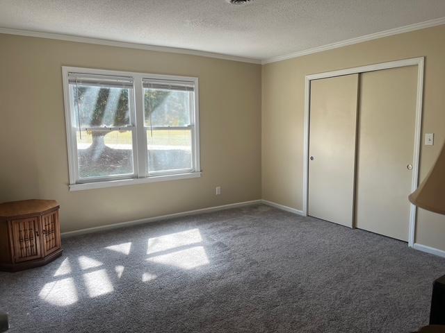 unfurnished bedroom with a textured ceiling, a closet, baseboards, and crown molding