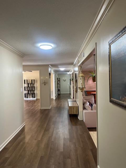 hall with a textured ceiling, ornamental molding, wood finished floors, and baseboards