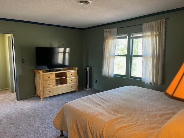 bedroom featuring crown molding, a textured ceiling, visible vents, and carpet flooring