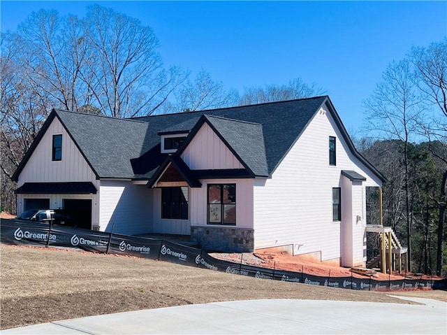 modern inspired farmhouse with a garage, stone siding, roof with shingles, and board and batten siding