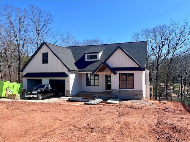 modern farmhouse with driveway, stone siding, a shingled roof, and a garage