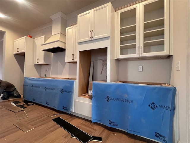 kitchen featuring light wood finished floors, custom exhaust hood, glass insert cabinets, and white cabinets