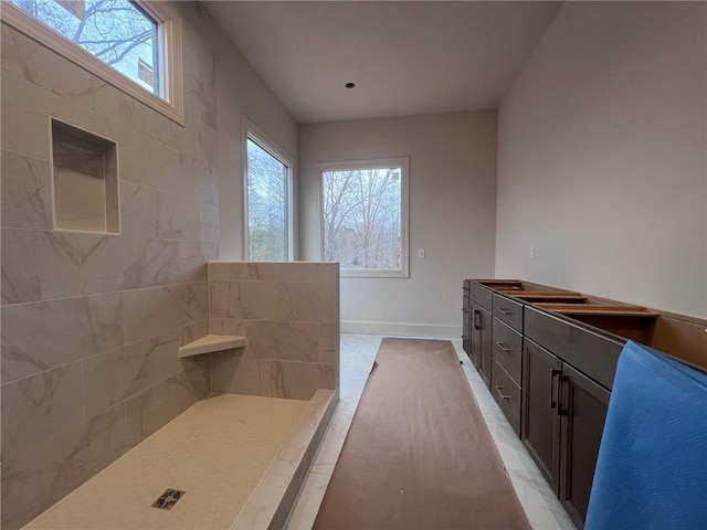 full bathroom with a wealth of natural light, marble finish floor, tiled shower, and baseboards