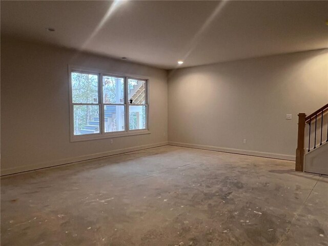 unfurnished room with stairway, unfinished concrete flooring, and baseboards