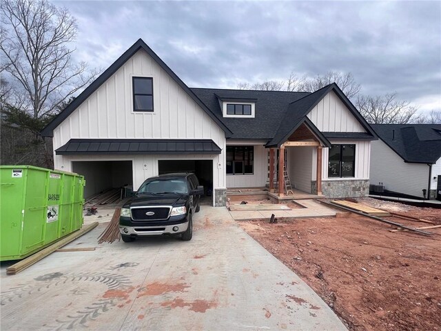 modern farmhouse featuring metal roof, concrete driveway, stone siding, roof with shingles, and board and batten siding