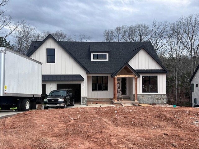 modern inspired farmhouse featuring an attached garage, stone siding, a shingled roof, and board and batten siding