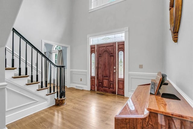 foyer featuring wainscoting, a decorative wall, stairway, and wood finished floors