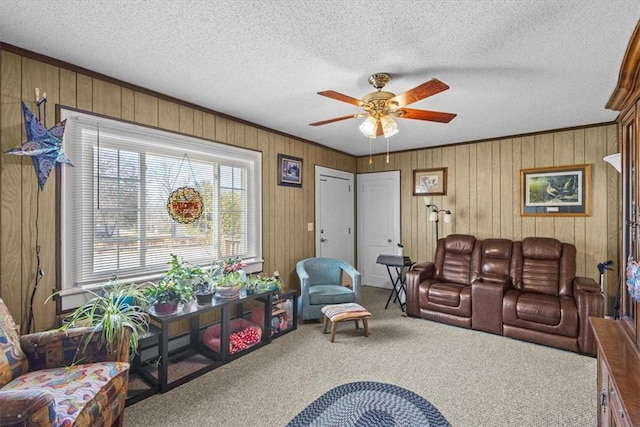 living room with ceiling fan, a textured ceiling, wooden walls, carpet floors, and ornamental molding