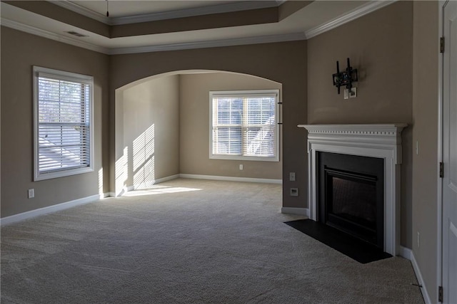 unfurnished living room featuring visible vents, a fireplace with flush hearth, a tray ceiling, crown molding, and carpet floors