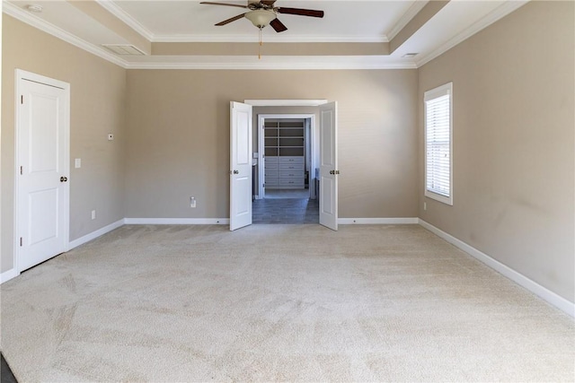 spare room featuring a raised ceiling, light colored carpet, crown molding, and baseboards