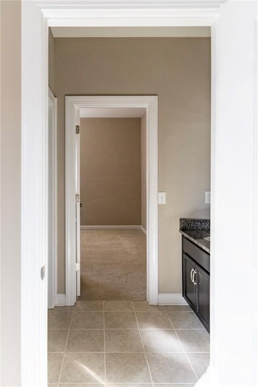 hallway with baseboards, light tile patterned flooring, and light colored carpet