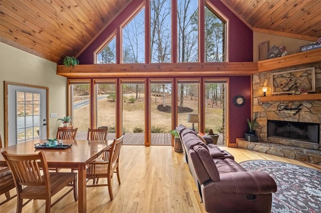 living area featuring light wood-type flooring, wood ceiling, high vaulted ceiling, and a stone fireplace