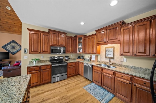 kitchen with recessed lighting, a sink, appliances with stainless steel finishes, light stone countertops, and light wood finished floors