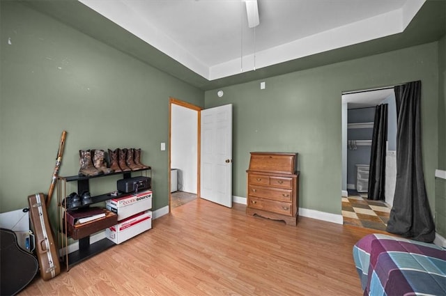 bedroom with a raised ceiling, ceiling fan, baseboards, and wood finished floors