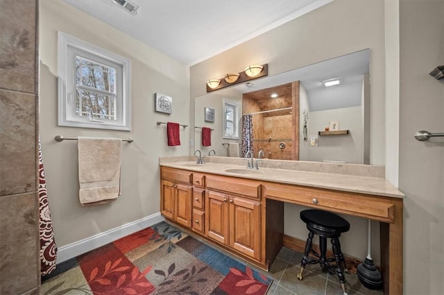 bathroom with a tile shower, double vanity, a sink, and baseboards