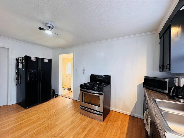 kitchen with stainless steel appliances, dark countertops, a sink, a textured ceiling, and light wood-type flooring