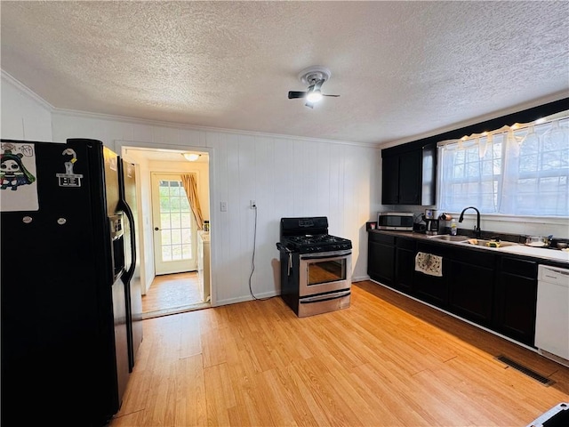 kitchen featuring stainless steel appliances, visible vents, light wood-style floors, a sink, and dark cabinetry