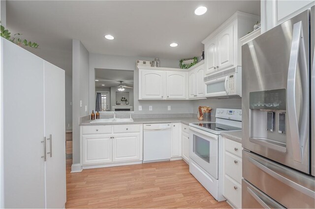 kitchen featuring light wood finished floors, light countertops, white cabinets, white appliances, and a sink