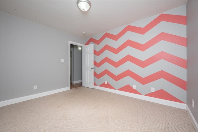 spare room with carpet flooring, an accent wall, and baseboards