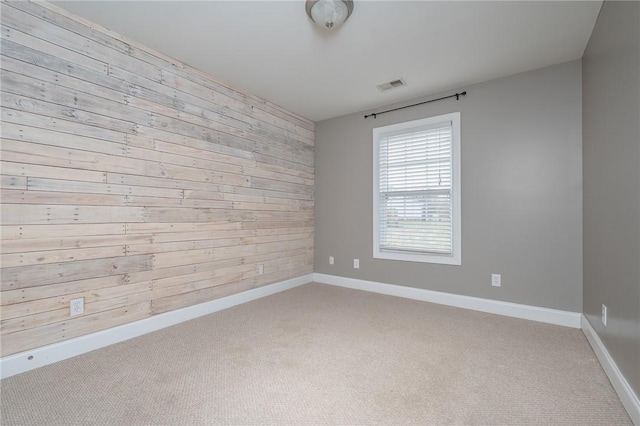 carpeted empty room with wooden walls, visible vents, and baseboards