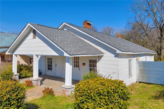 view of front of home featuring covered porch, a chimney, and roof with shingles