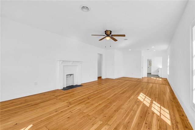 unfurnished living room with light wood finished floors, visible vents, ceiling fan, baseboards, and a fireplace with flush hearth