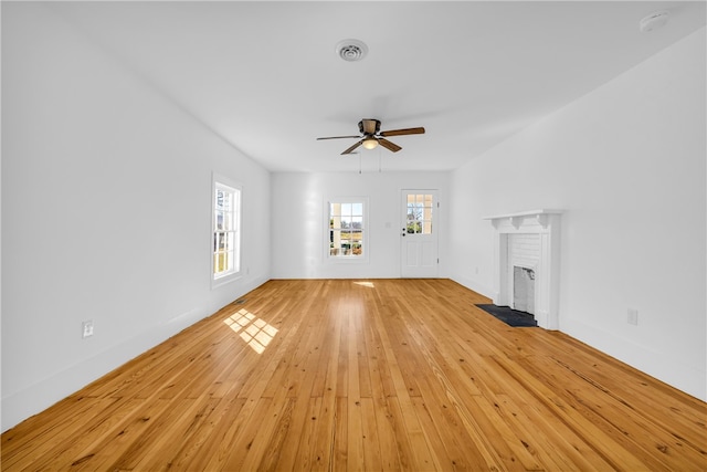 unfurnished living room with visible vents, light wood-style flooring, a ceiling fan, baseboards, and a brick fireplace