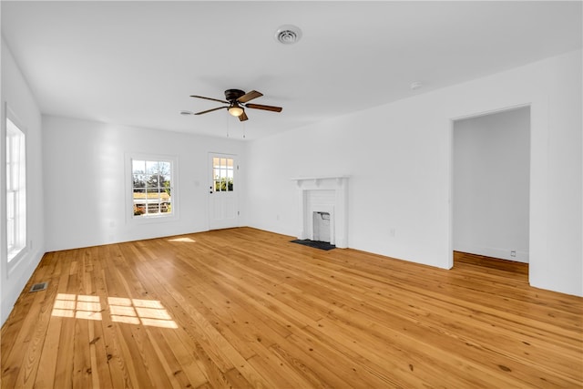 unfurnished living room featuring visible vents, a ceiling fan, a fireplace, and light wood finished floors