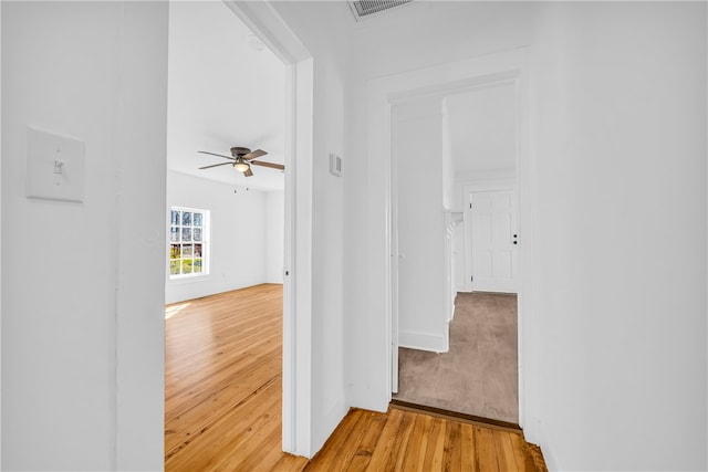 hall featuring visible vents, baseboards, and light wood finished floors