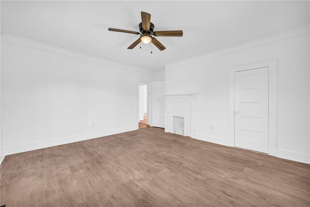 unfurnished living room with a ceiling fan, wood finished floors, baseboards, a fireplace, and ornamental molding