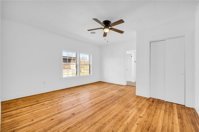 unfurnished bedroom featuring a ceiling fan, visible vents, baseboards, light wood-style flooring, and a closet