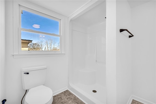 bathroom with toilet, a shower, and baseboards