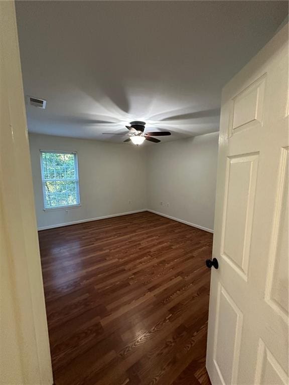 empty room featuring ceiling fan, visible vents, baseboards, and dark wood-style floors