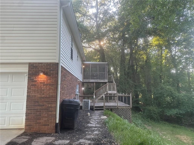 view of side of property with cooling unit, an attached garage, a sunroom, a deck, and brick siding