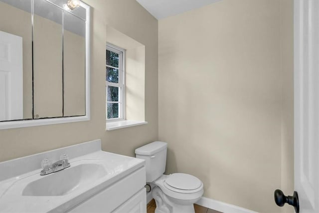 half bathroom featuring baseboards, toilet, and vanity