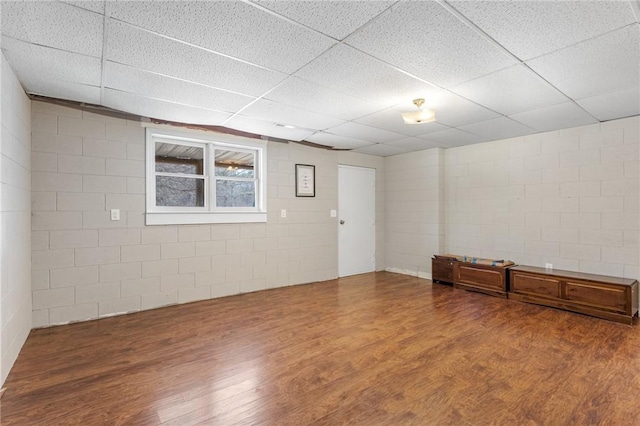 unfurnished room with a drop ceiling, concrete block wall, and wood finished floors