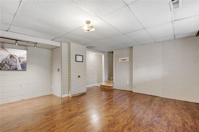 finished below grade area with visible vents, a paneled ceiling, wood finished floors, and concrete block wall