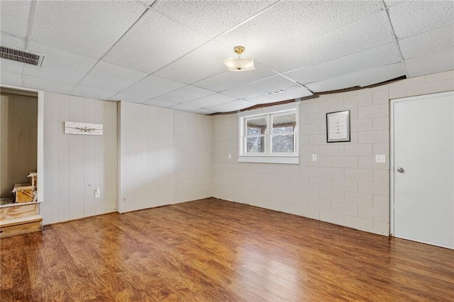 below grade area with a drop ceiling, visible vents, wood finished floors, and concrete block wall