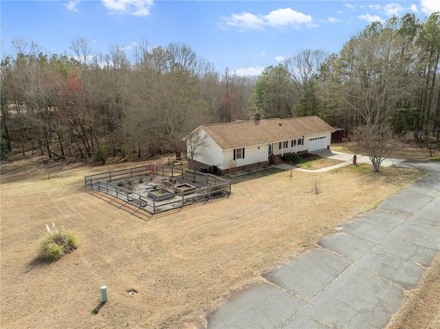 view of front facade featuring fence, driveway, a garden, a garage, and a view of trees