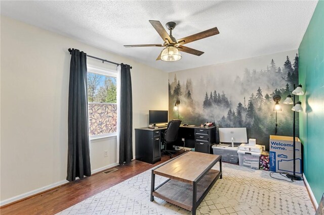 home office featuring wood finished floors, visible vents, baseboards, ceiling fan, and a textured ceiling