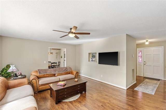 living area featuring ceiling fan, a textured ceiling, baseboards, and wood finished floors