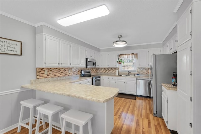 kitchen featuring light countertops, ornamental molding, appliances with stainless steel finishes, a peninsula, and white cabinets