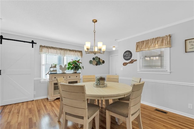 dining area featuring visible vents, a wainscoted wall, a barn door, light wood-style floors, and an inviting chandelier