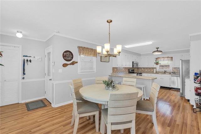 dining room featuring light wood-style flooring, baseboards, an inviting chandelier, and ornamental molding