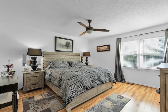 bedroom with baseboards, a textured ceiling, light wood-style flooring, and a ceiling fan