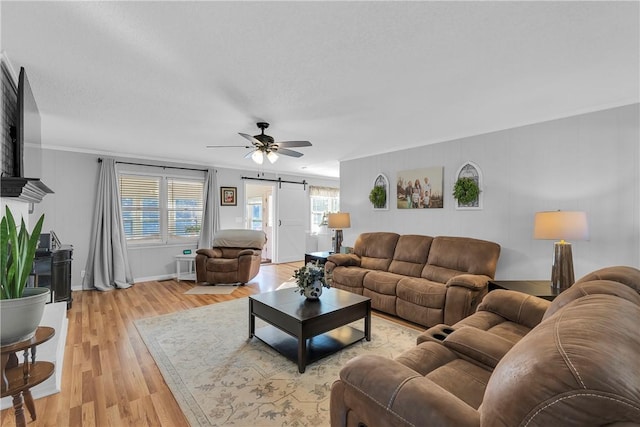 living area with a barn door, ornamental molding, light wood finished floors, and ceiling fan