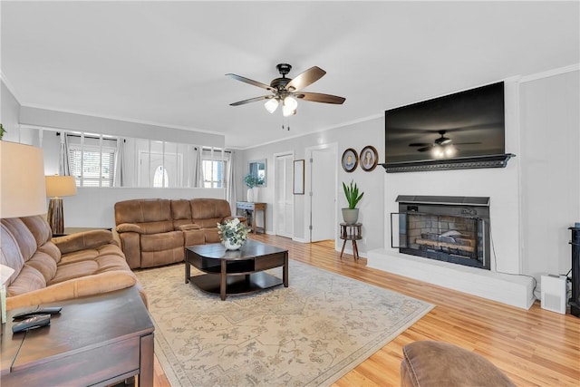 living area featuring a fireplace with raised hearth, wood finished floors, ceiling fan, and ornamental molding