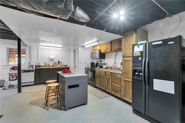 kitchen featuring black appliances, a kitchen island, brown cabinetry, concrete block wall, and concrete flooring