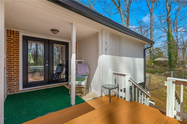 view of exterior entry featuring brick siding, french doors, and fence